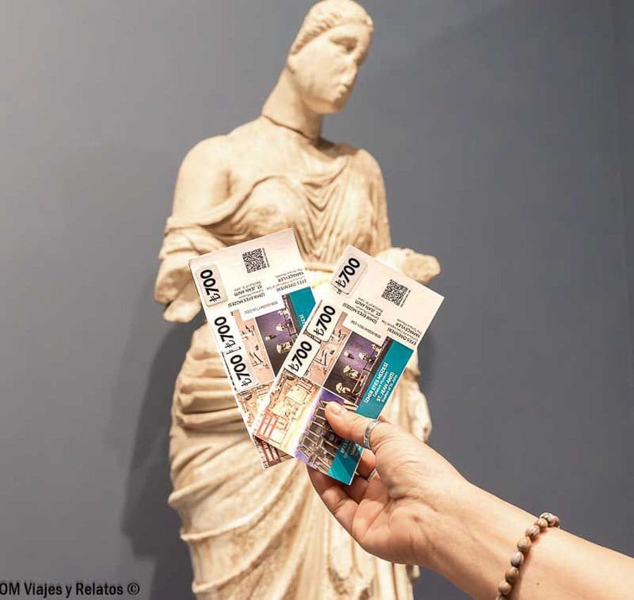 Olga mostrando las entradas del museo de Éfeso delante de una estatua, detalle útil en que ver en Efeso.