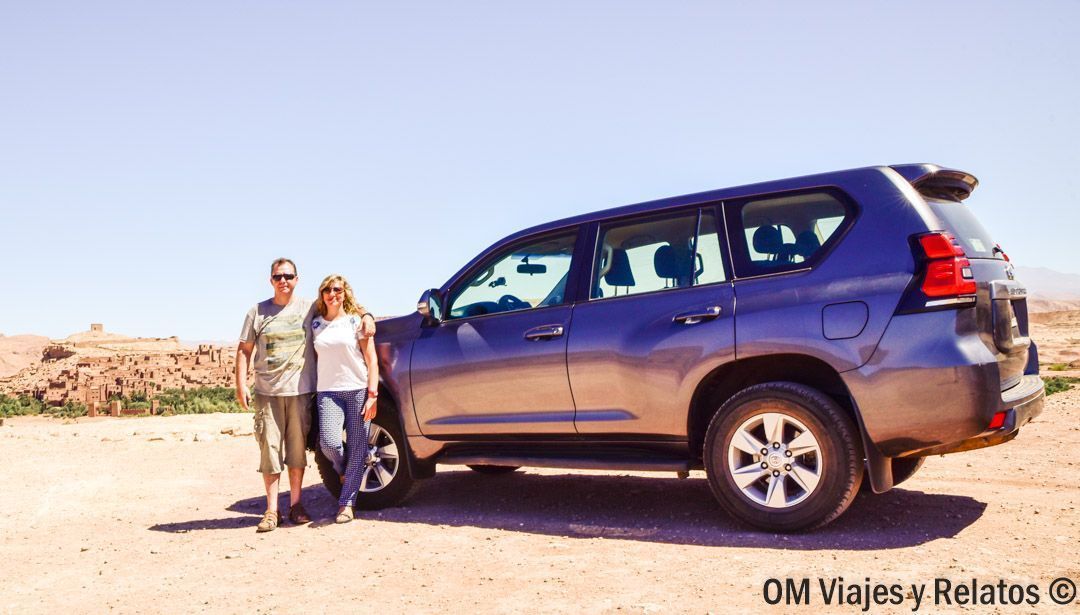 Pareja OM Viajes y Relatos posando junto a un 4x4 en un paisaje árido, durante rutas en coche por Marruecos.