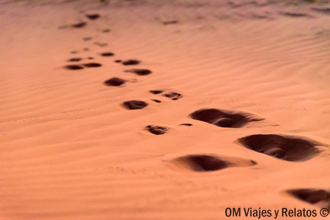 Ruta por Marruecos en coche: huellas en la arena de las dunas del desierto, primer plano con tonos anaranjados.