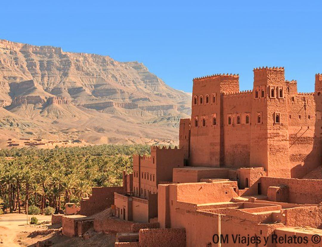 Kasbah de adobe junto a un palmeral con montañas del Atlas al fondo, paisaje clave en una ruta por Marruecos en coche.