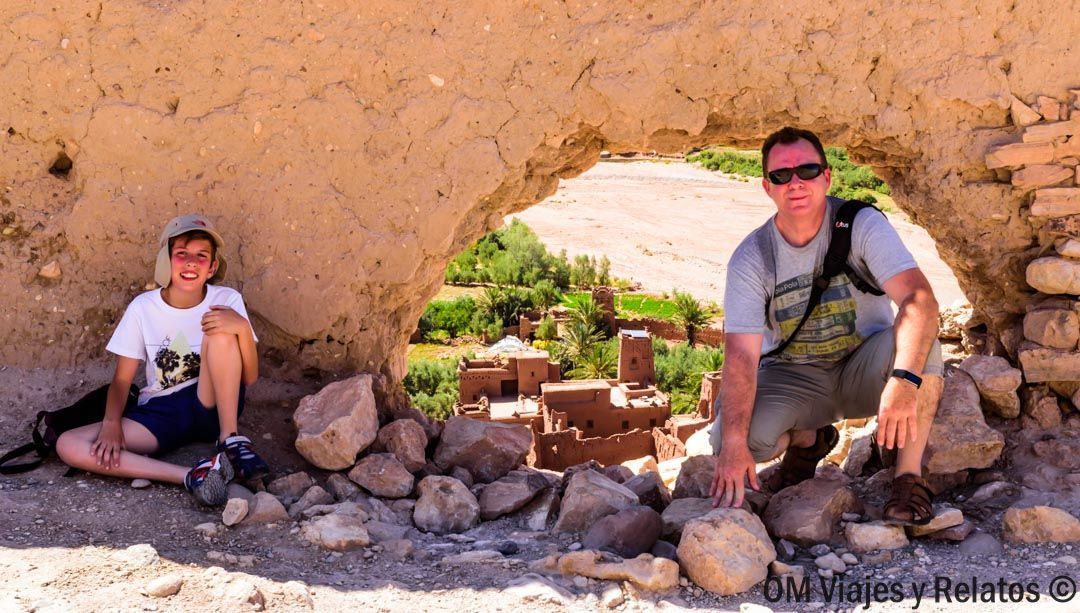 JC y nuestro hijo en una abertura de roca con vistas a una kasbah, momento épico en una ruta por Marruecos en coche