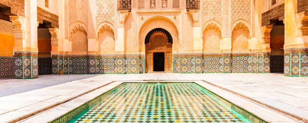 Patio con mosaicos zellige y una alberca central en una madrasa de Marruecos, una visita típica en rutas en coche por Marruecos.