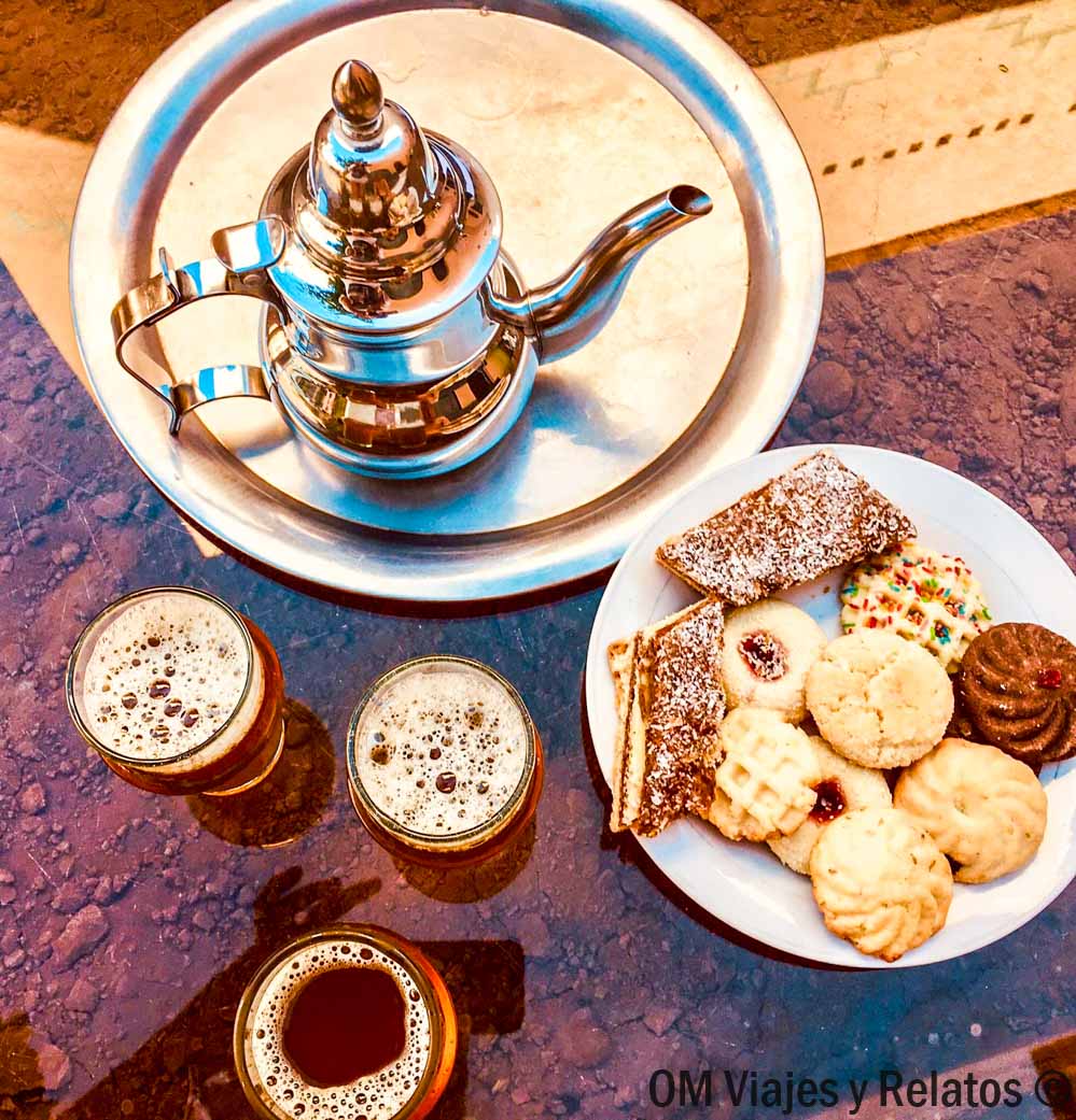 Tetera con vasos de té marroquí y un plato de dulces típicos, una pausa deliciosa en rutas en coche por Marruecos.