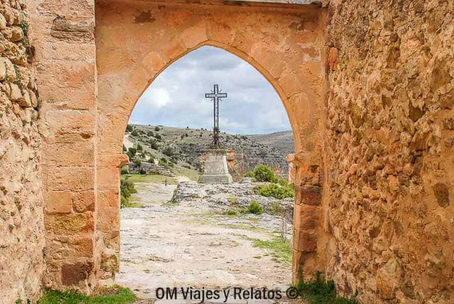 Arco de piedra con una cruz y paisaje del cañón en las Hoces del Río Duratón, una parada con encanto para descubrir rutas en Castilla y León.