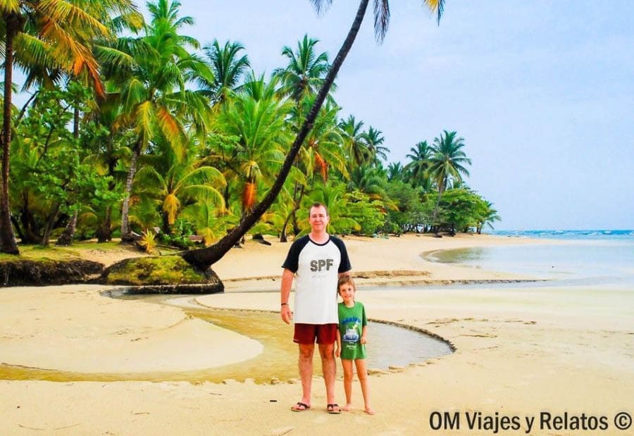 JC e hijo posando en la orilla con palmeras y agua tranquila, disfrutando en familia de las playas de Samana.