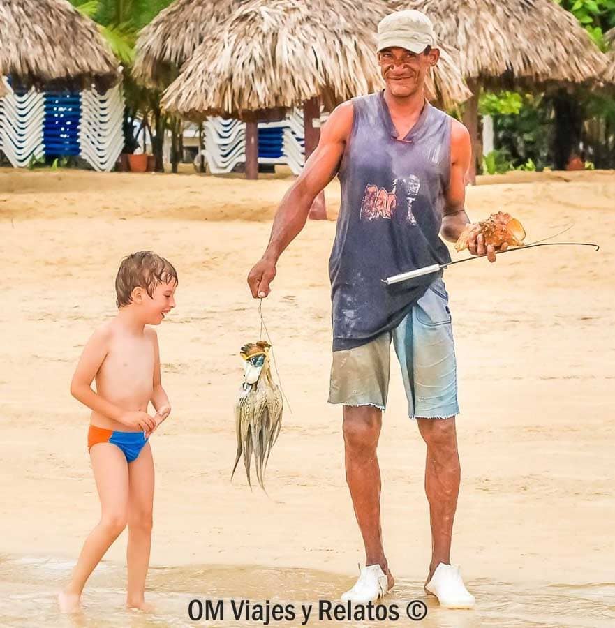Raúl en la orilla mirando a un pescador con la pesca del día, una escena auténtica en las playas de Samana.