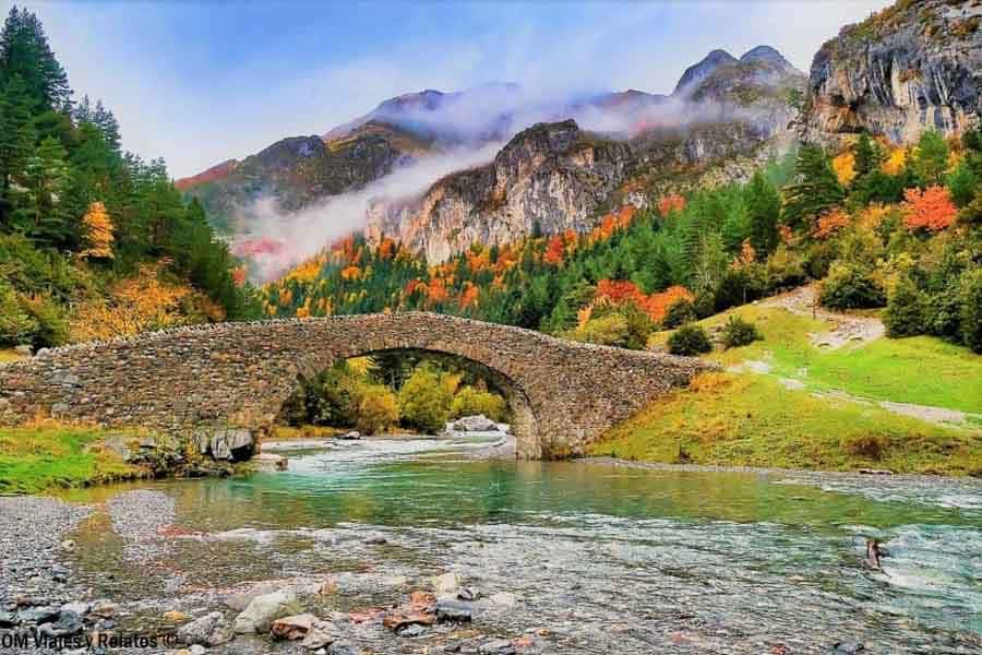 Puente de piedra sobre el río con bosque en otoño, una escena imprescindible de que ver en Ordesa y Monte Perdido.