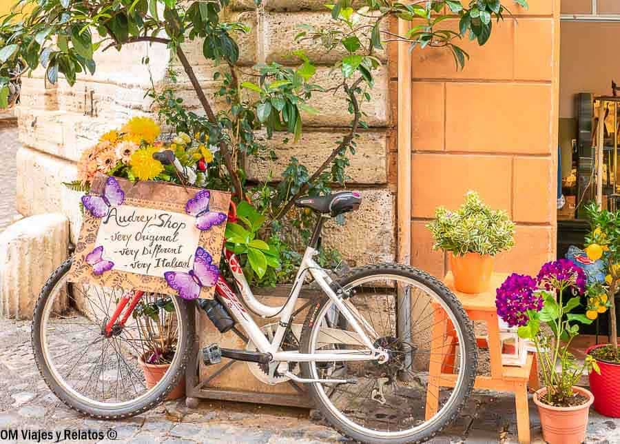 Bicicleta apoyada junto a flores y una tienda con encanto, un rincón bonito en que ver en Roma en 4 días.