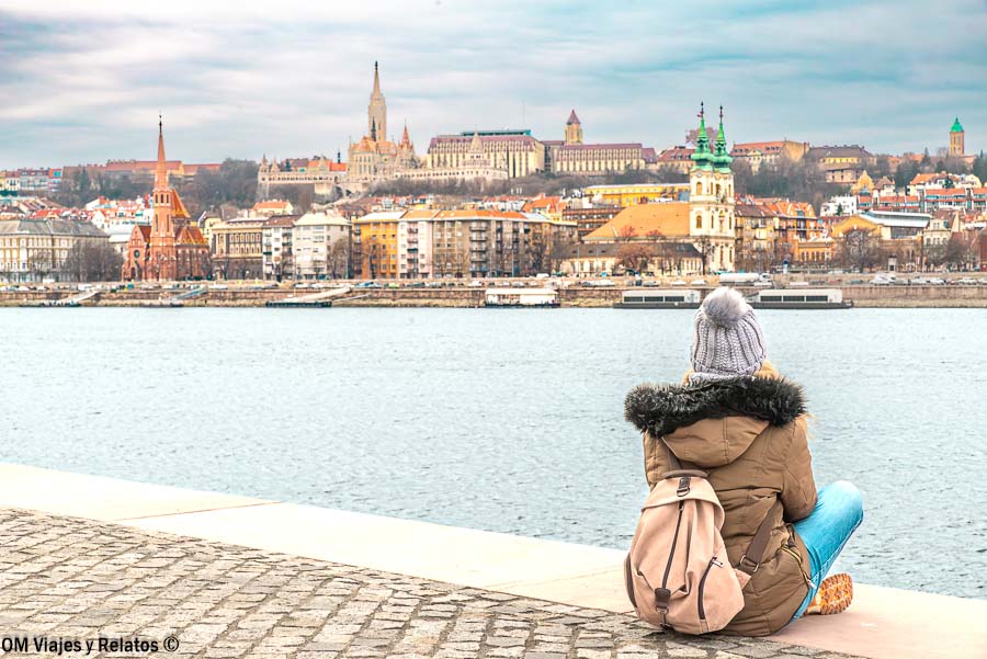 Olga sentada junto al Danubio con vistas a Buda al fondo, una imagen perfecta para completar un paseo en barco Budapest