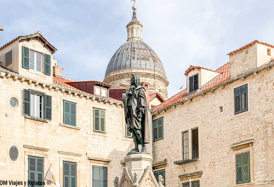Estatua histórica en el casco antiguo de Dubrovnik con la cúpula de la catedral al fondo durante una ruta por Croacia en 7 días.