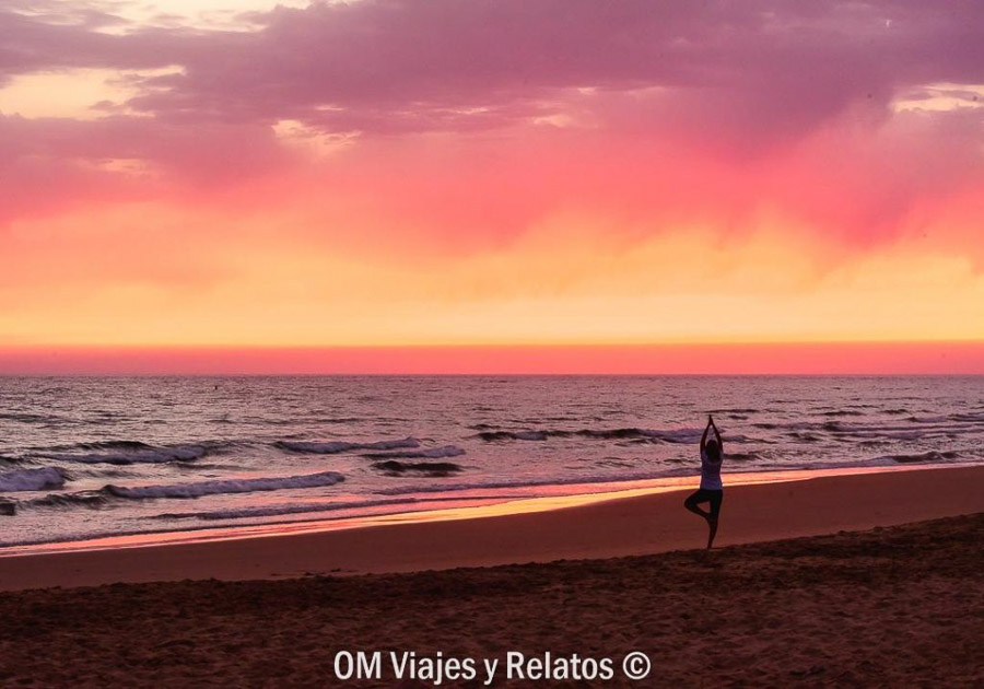 Persona haciendo yoga al atardecer en una de las playas mas bonitas de Cádiz con el cielo rosado sobre el mar.