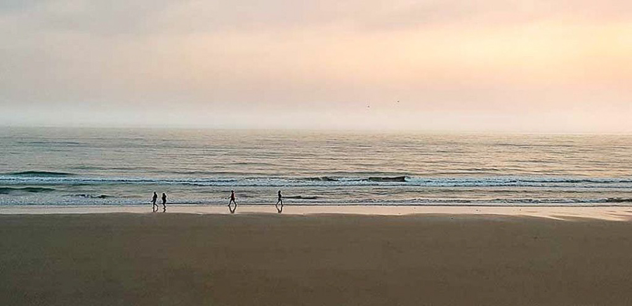 Personas paseando al atardecer en una de las playas mas bonitas de Cádiz con el mar en calma.