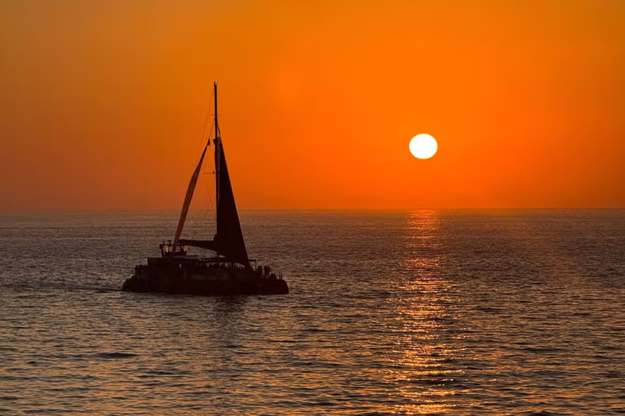 Velero al atardecer en una de las playas mas bonitas de Cadiz con el sol reflejado en el mar.