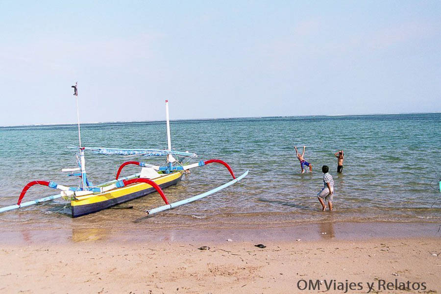 Barco tradicional en la playa de Sanur con personas bañándose en el mar, una zona tranquila para incluir al planificar qué ver y hacer en Bali por zonas.