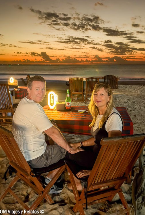 Foto en pareja de OM Viajes y Relatos cenando frente al mar al atardecer en Jimbaran Beach, una experiencia romántica en una de las mejores playas de Bali.