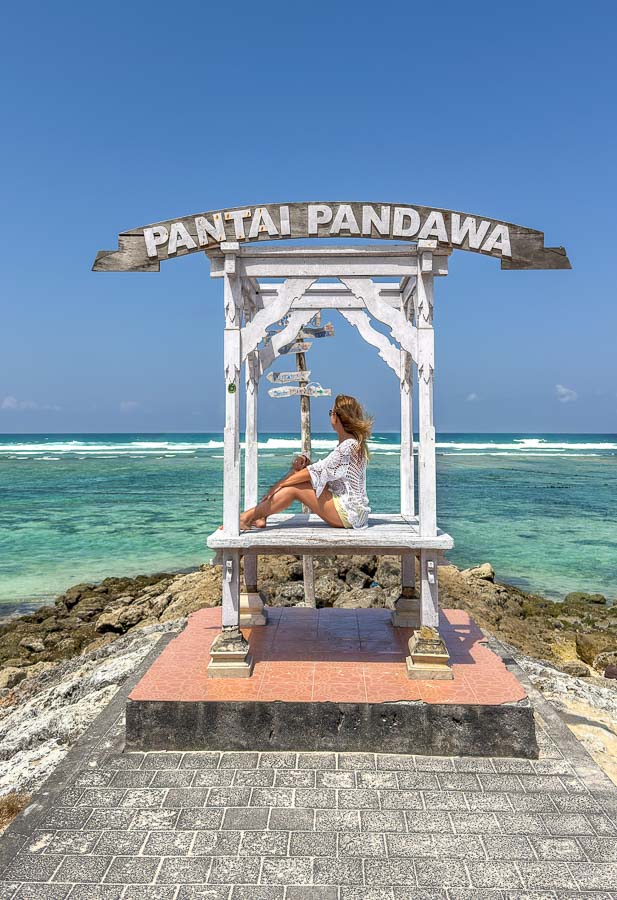 Servidora posando bajo el cartel de Pantai Pandawa frente al mar, una parada imprescindible entre las mejores playas de Bali.