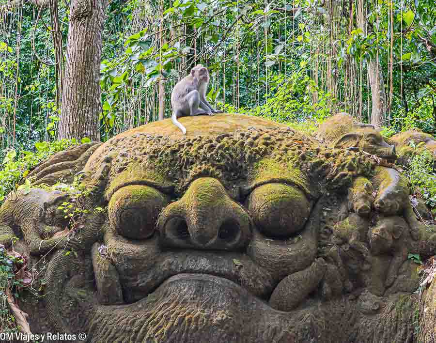 Mono sobre una escultura de piedra cubierta de musgo en el Bosque de los Monos de Ubud