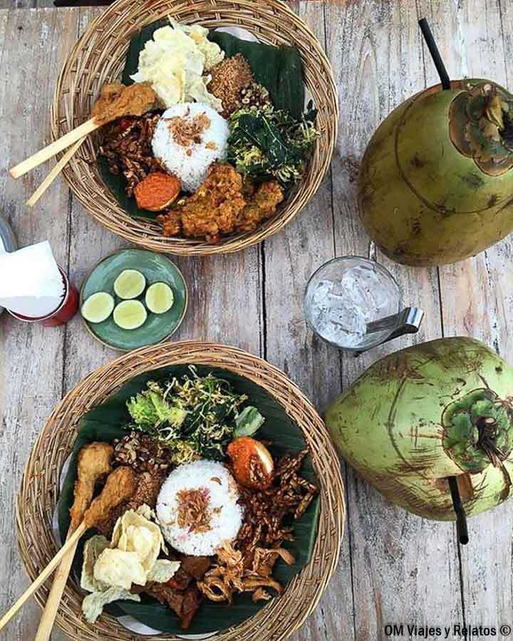 Nasi campur balinés con arroz, verduras y acompañamientos servido con coco fresco