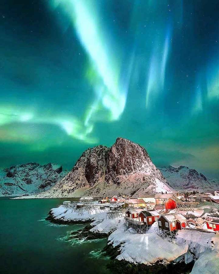 Aurora boreal sobre un pueblo pesquero y montañas nevadas de las islas Lofoten en Noruega