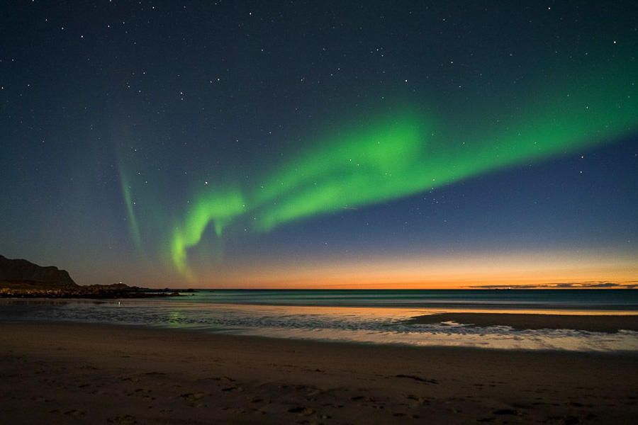 Aurora boreal verde sobre una playa y el mar en el norte de Noruega