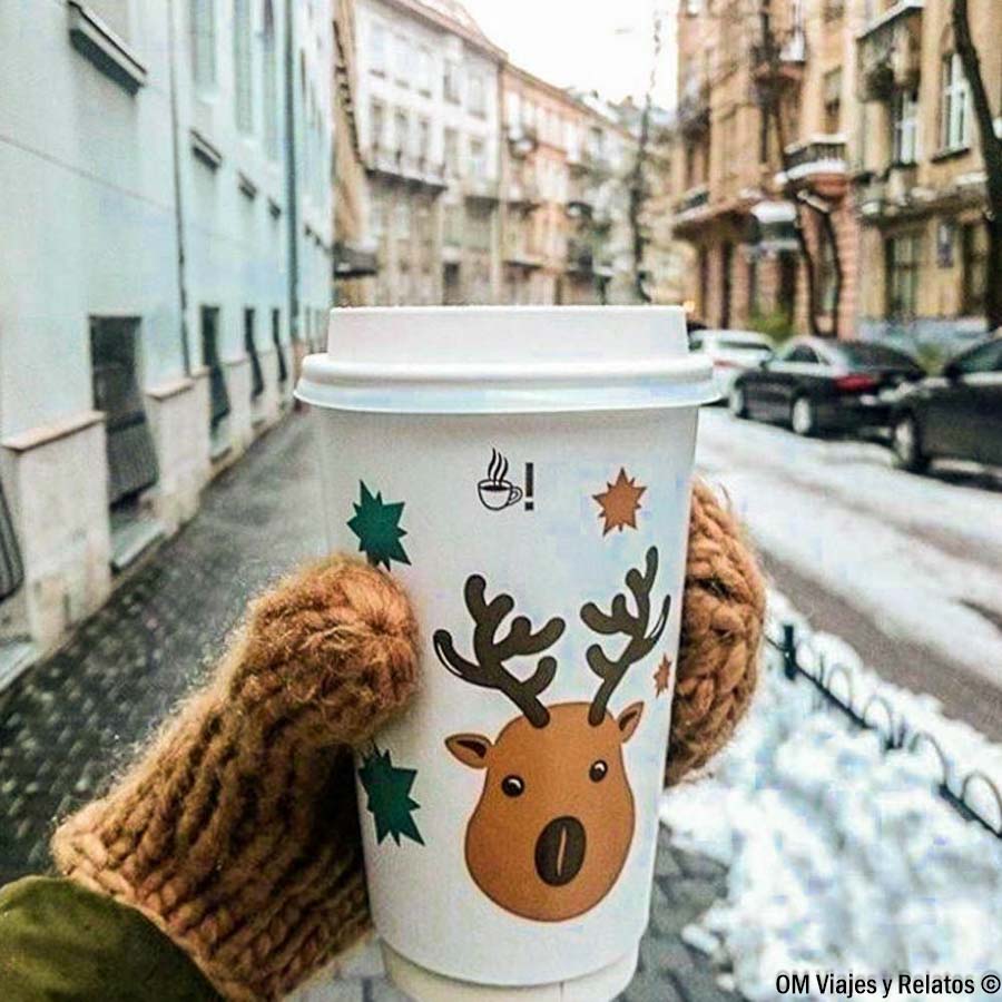 Vaso de bebida caliente con dibujo de reno en una calle nevada durante la Navidad