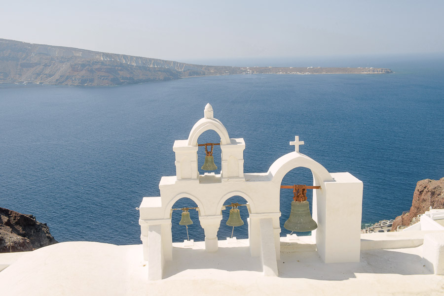 Campanario blanco de una iglesia de Santorini con vistas a la caldera y al mar Egeo