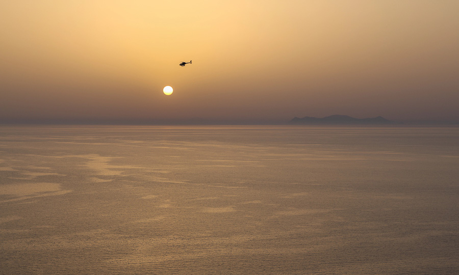 Helicóptero sobrevolando Santorini al atardecer sobre el mar Egeo