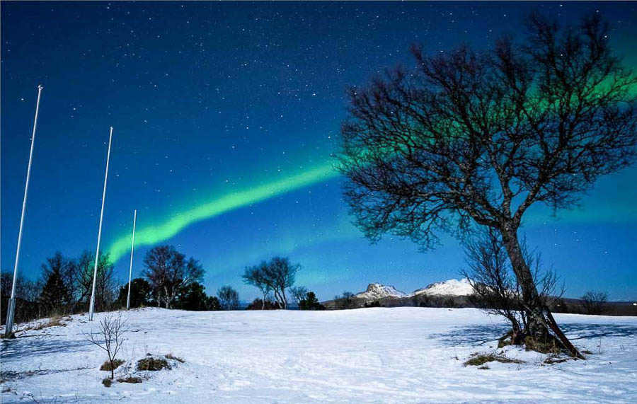 Aurora boreal verde sobre un paisaje nevado, uno de los lugares donde ver las auroras boreales en Noruega