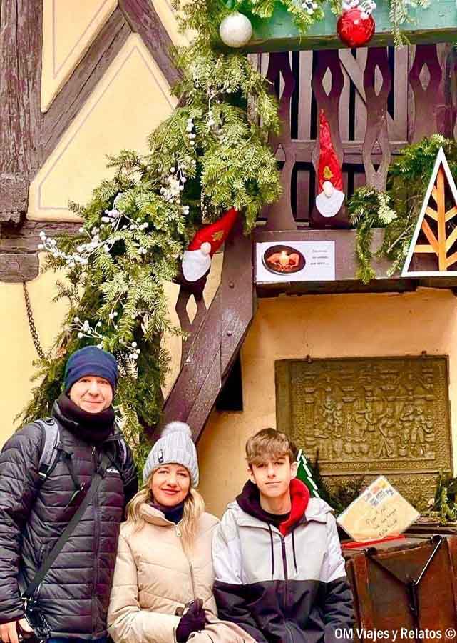Foto familiar de OM Viajes y Relatos frente a una casa alsaciana decorada con guirnaldas y adornos de Navidad