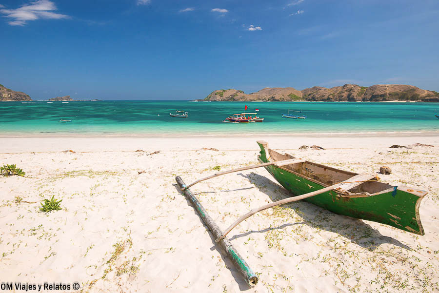 Playa de arena blanca y aguas turquesas con una embarcación tradicional en una de las islas de Indonesia