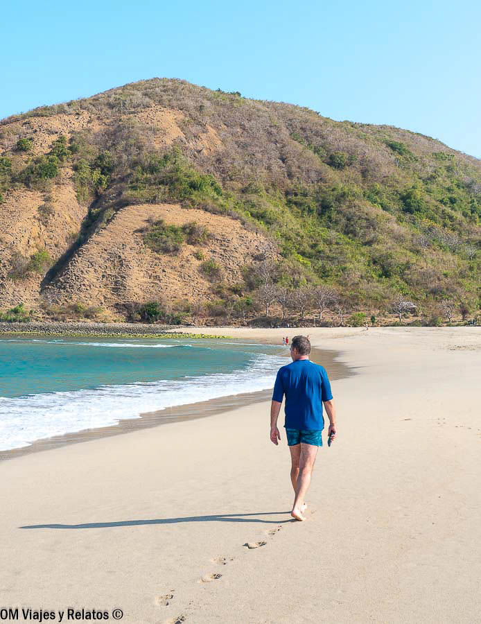 Playa de arena dorada y aguas turquesas en una de las islas de Indonesia, con JC paseando junto a la orilla