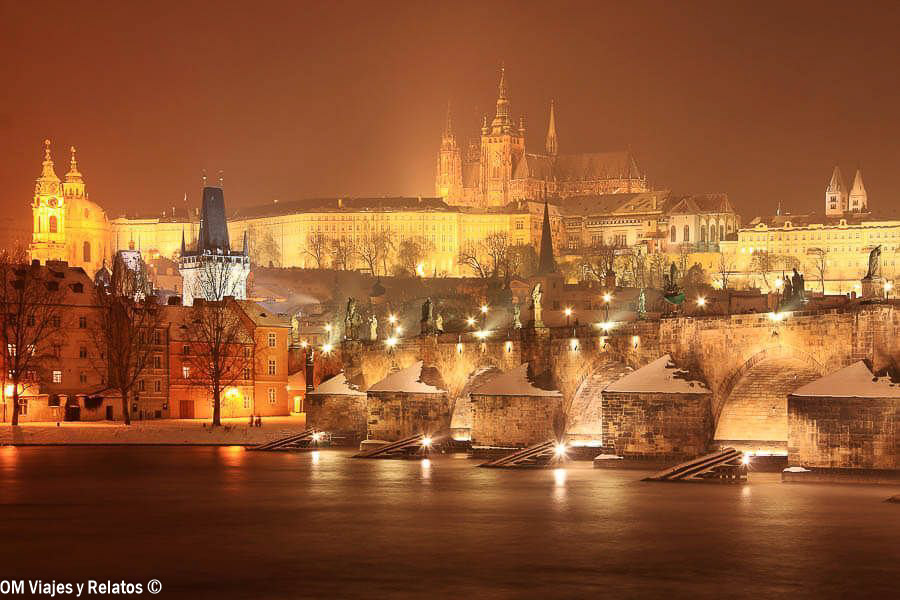 Puente de Carlos iluminado de noche con el Castillo de Praga al fondo
