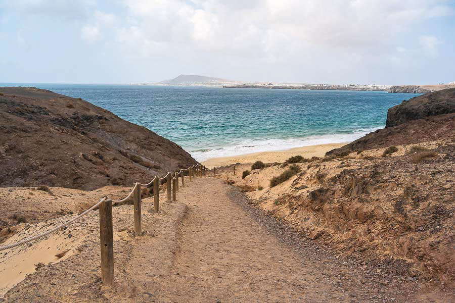 Sendero de tierra hacia una cala de Lanzarote con el mar y la costa al fondo