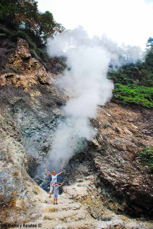 Foto mía y de mi hijo junto a una zona geotérmica en Indonesia, rodeados de vapor y paisaje volcánico