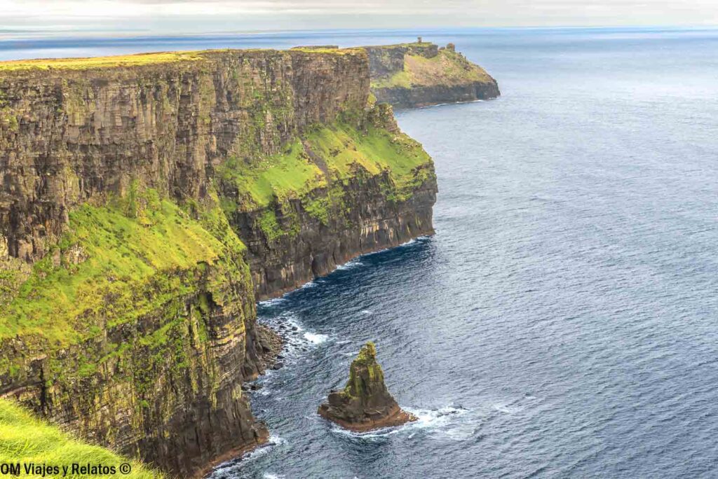 Impresionantes paredes rocosas de los Acantilados de Moher en Irlanda, con verdes laderas y un farallón emergiendo del océano Atlántico