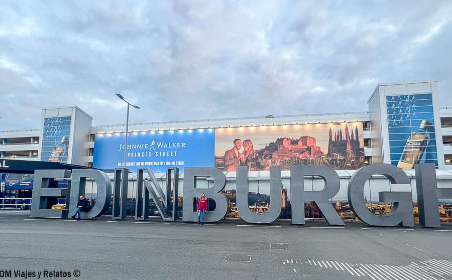 Una servidora junto al letrero de Edinburgh frente a la terminal del aeropuerto de Edimburgo
