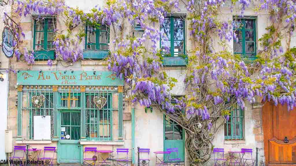 Fachada del restaurante Au Vieux Paris d’Arcole decorada con glicinias moradas y mesas de terraza en París