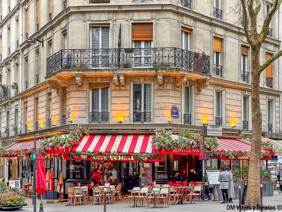 Terraza de una típica brasserie parisina, con toldos rojos y blancos, mesas al aire libre y una fachada decorada con flores