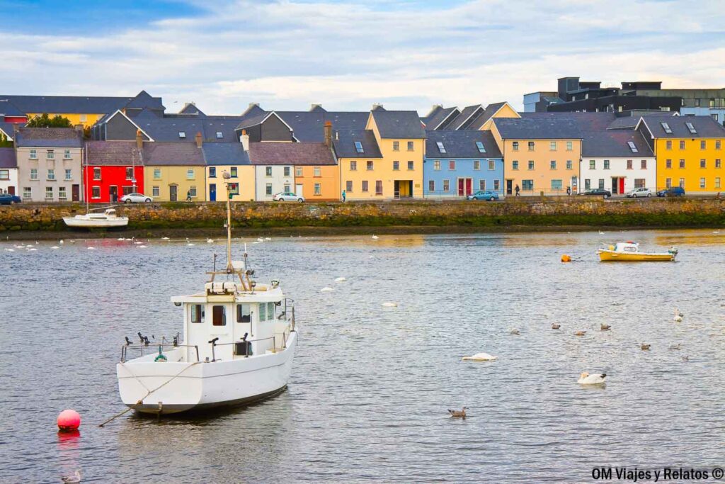 Casas de colores junto al puerto de Galway, con barcos de pesca y aves marinas sobre el agua