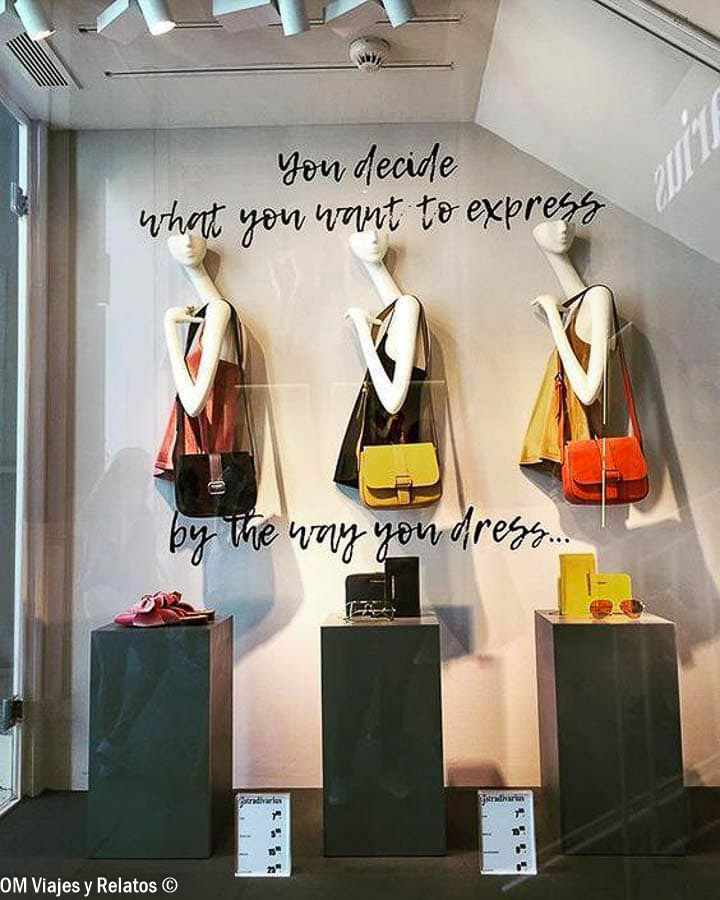 Escaparate de una tienda de moda en Madrid, con tres maniquíes, bolsos de colores y una frase decorativa en inglés