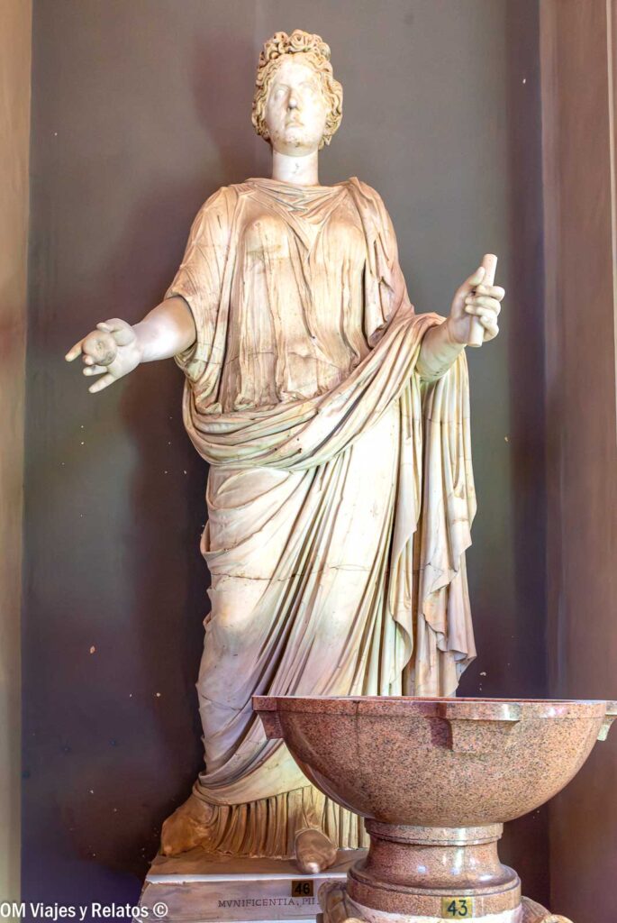 Estatua clásica de una figura femenina con túnica y un recipiente de piedra en una sala de los Museos Vaticanos