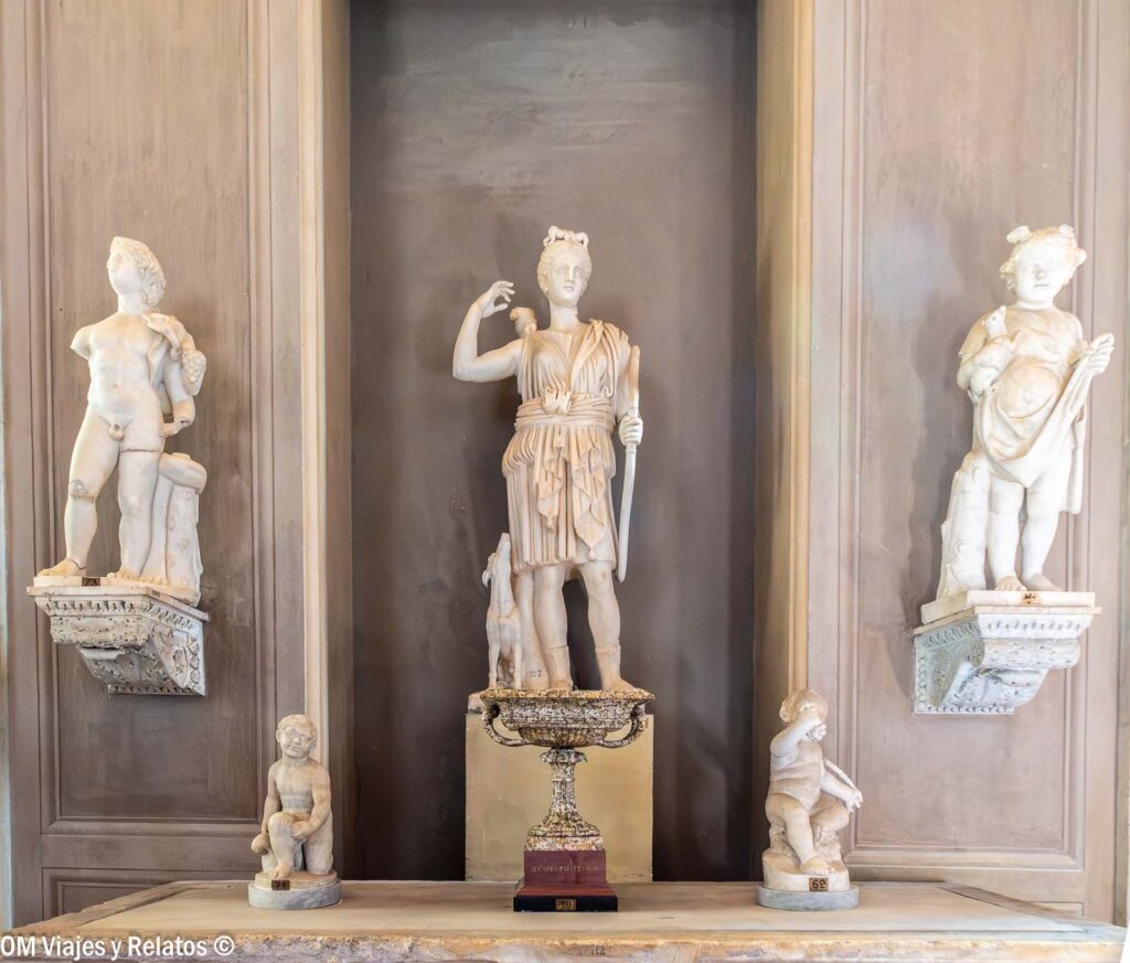 Conjunto de esculturas clásicas de mármol en los Museos Vaticanos, con una figura femenina en el centro y varias estatuas alrededor