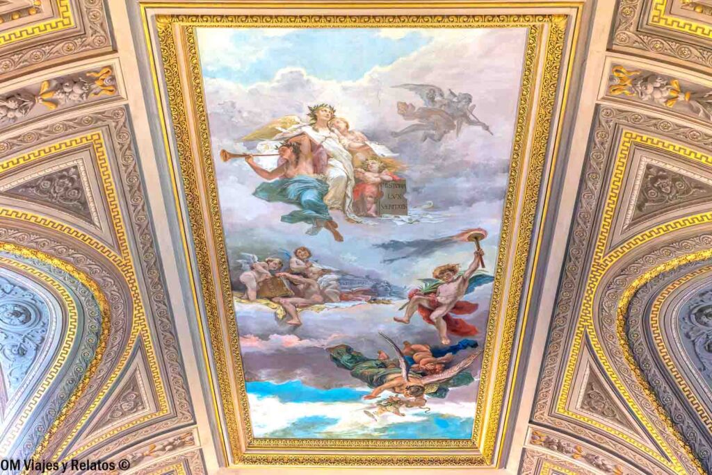 Fresco alegórico con figuras entre las nubes y molduras doradas en el techo de una galería de los Museos Vaticanos