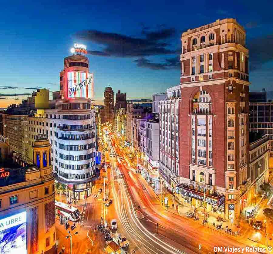 Vista panorámica de la Gran Vía de Madrid al anochecer, con el edificio Capitol y su luminoso cartel de Schweppes