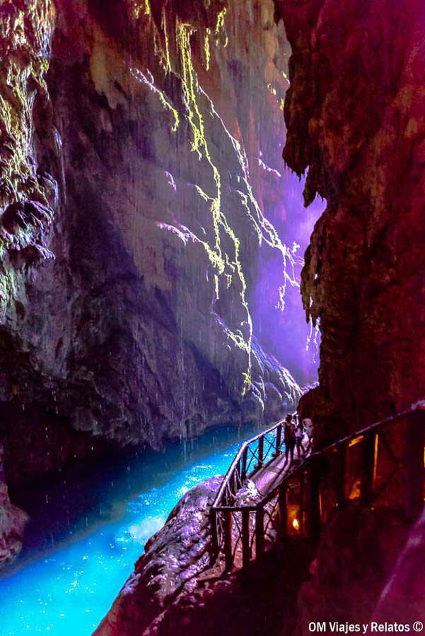 Interior de la Gruta Iris del Monasterio de Piedra, con una pasarela de madera junto al agua turquesa y paredes rocosas