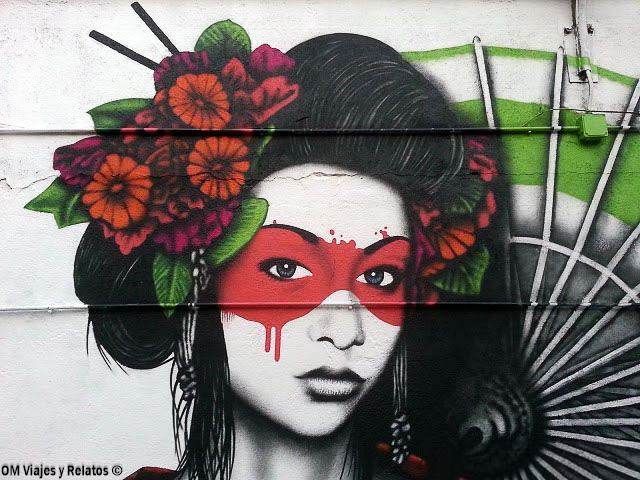Mural de arte urbano en La Tabacalera de Madrid, con el rostro de una mujer, flores de colores y un abanico japonés