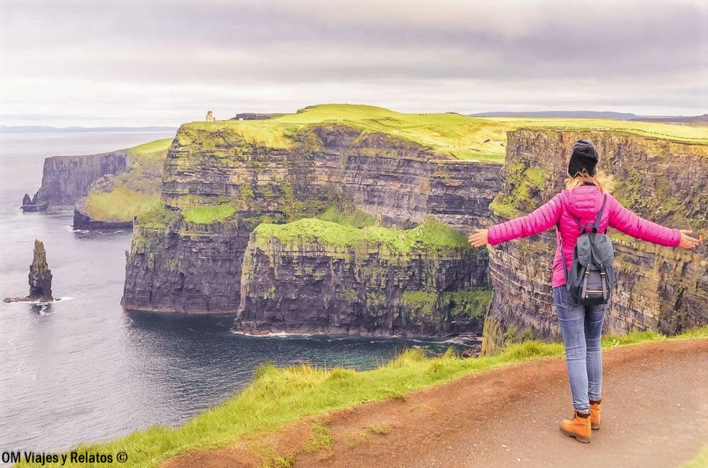 Una servidora contemplando los Acantilados de Moher en Irlanda con los brazos abiertos frente a las enormes paredes de roca y el océano Atlántico