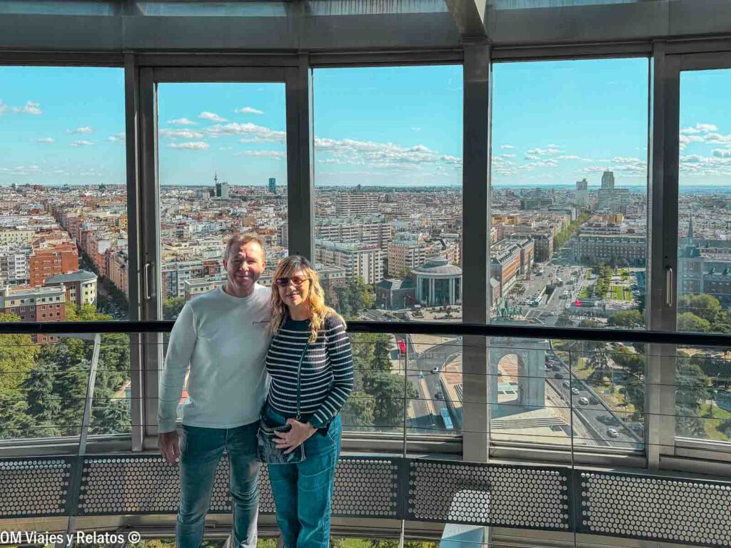 Foto en pareja de OM Viajes y Relatos en el mirador del Faro de Moncloa, disfrutando de las vistas panorámicas de Madrid a través de sus grandes ventanales