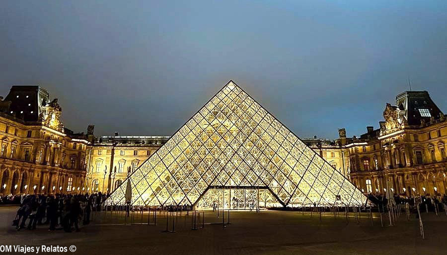 Pirámide de cristal del Museo del Louvre iluminada de noche, rodeada por las fachadas históricas del palacio en París
