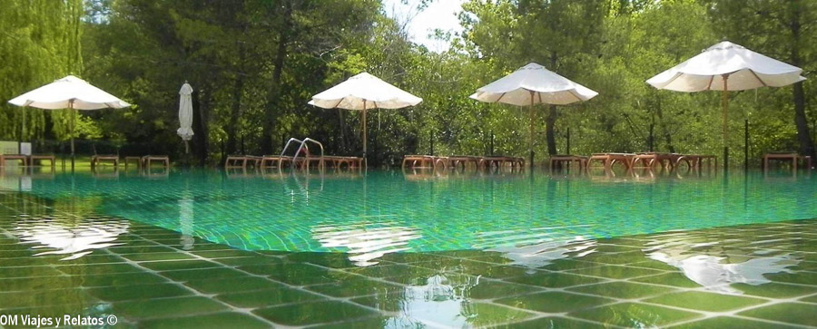 Piscina exterior del Hotel Monasterio de Piedra, rodeada de árboles y con sombrillas y tumbonas junto al agua